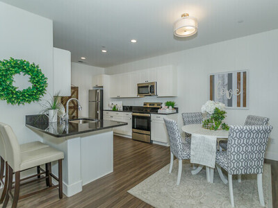 Photo of a vacant unit shows dark wood floors, an open concept kitchen, and a brief view into the restroom